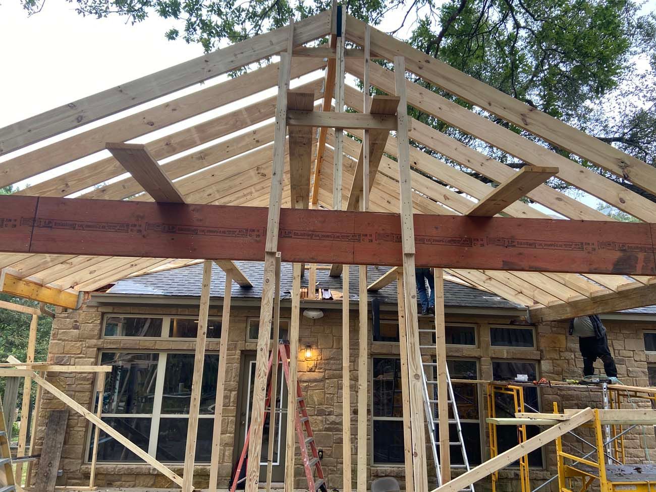 Construction workers building a wooden roof frame over a stone building.