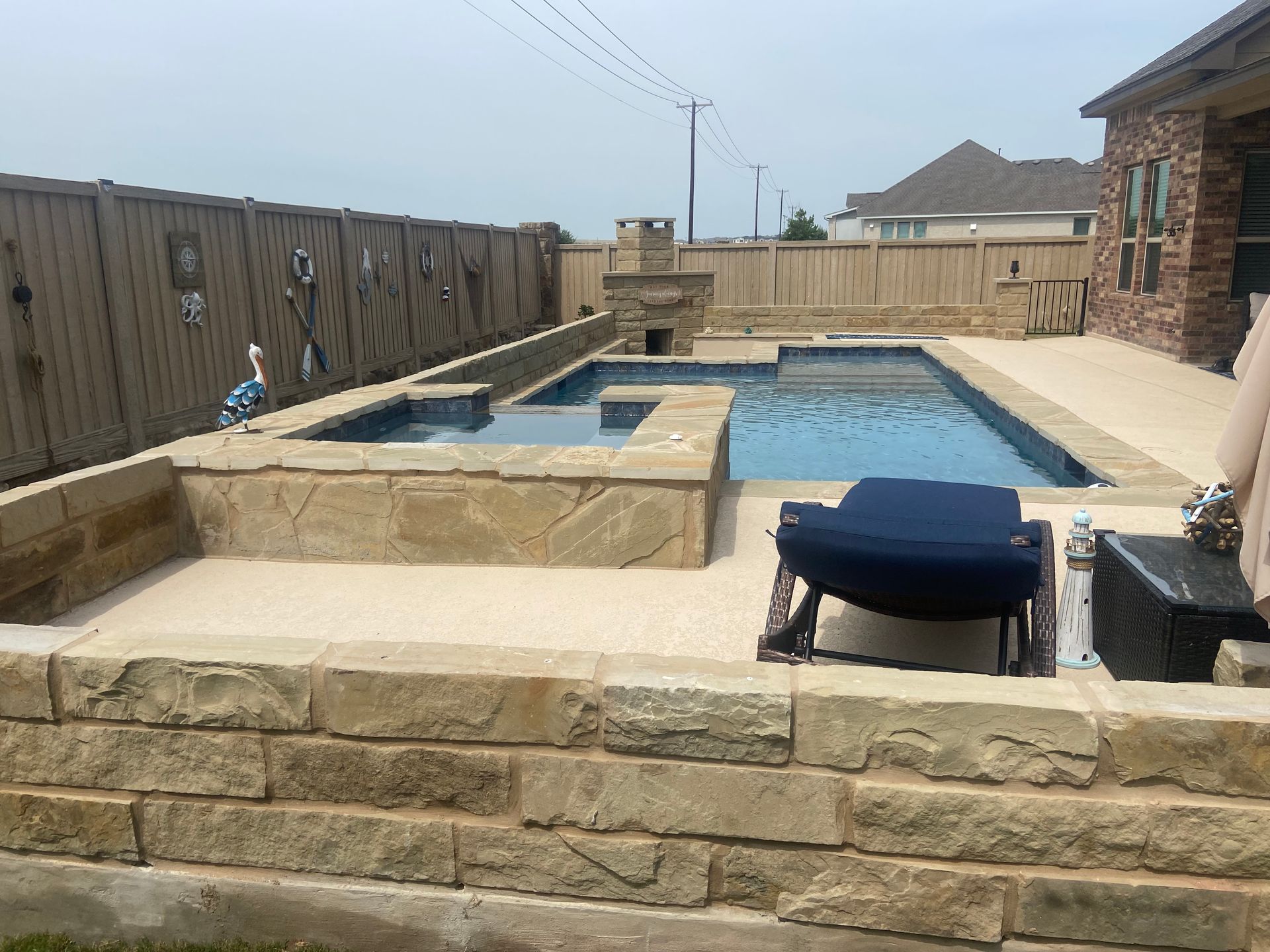 Swimming pool with spa and stone features, surrounded by a fence and patio.
