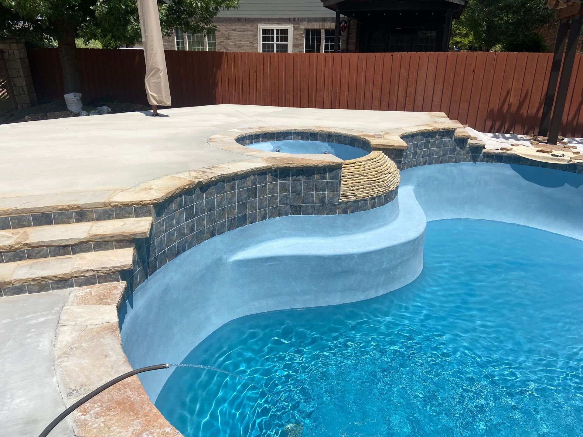 Swimming pool with steps, a raised spa, and cascading water. Clear blue water and gray concrete.