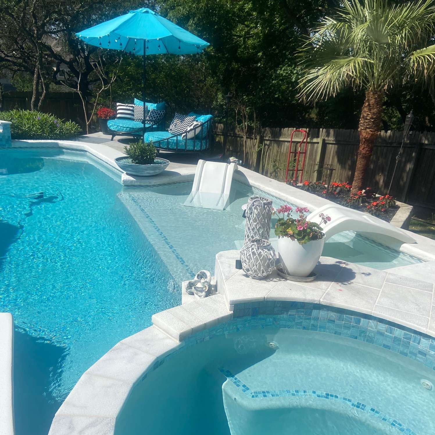 A luxurious backyard pool with a hot tub, slide, and seating area; turquoise and white decor.
