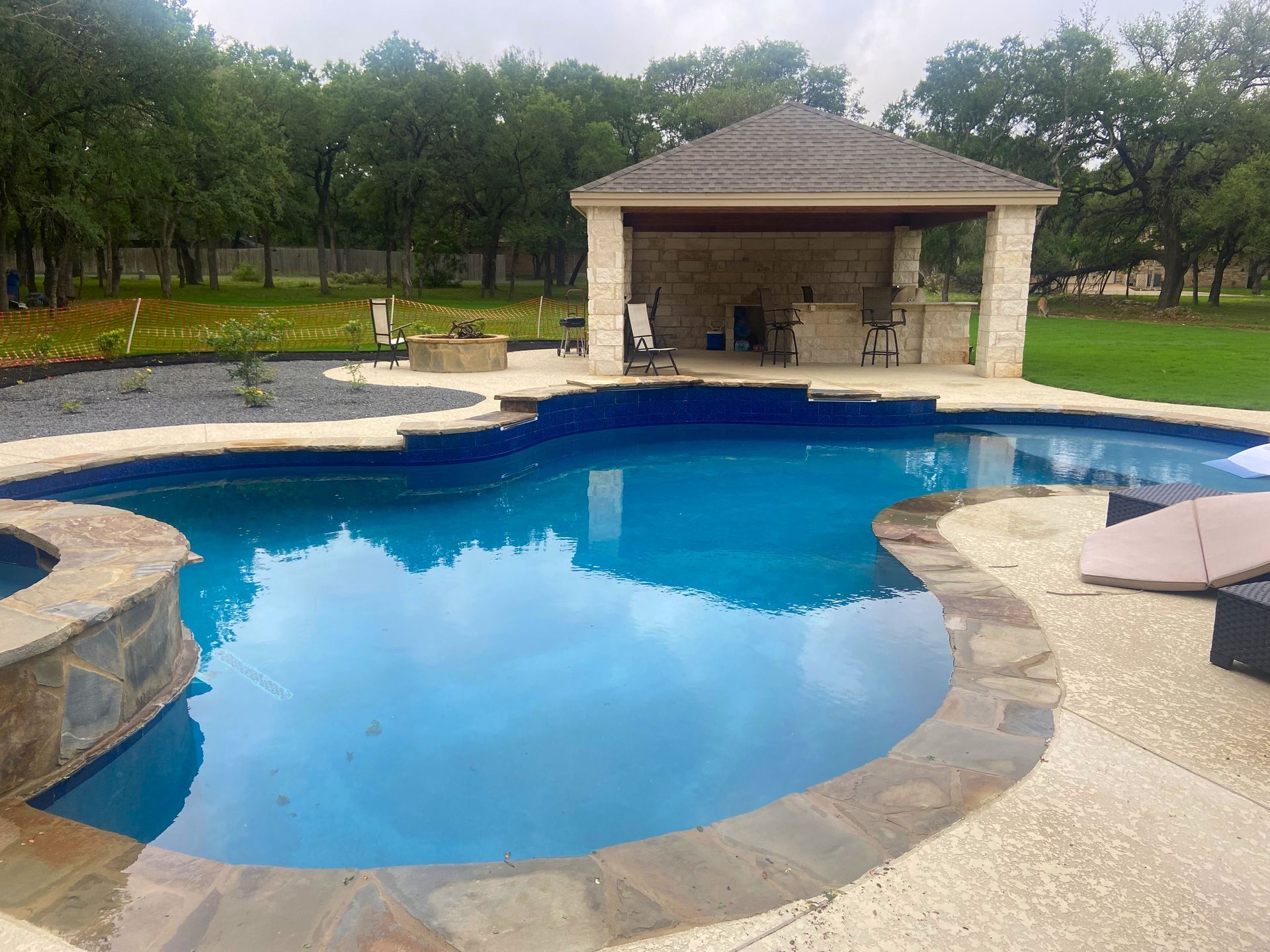 Swimming pool with a gazebo and outdoor kitchen in a backyard setting.