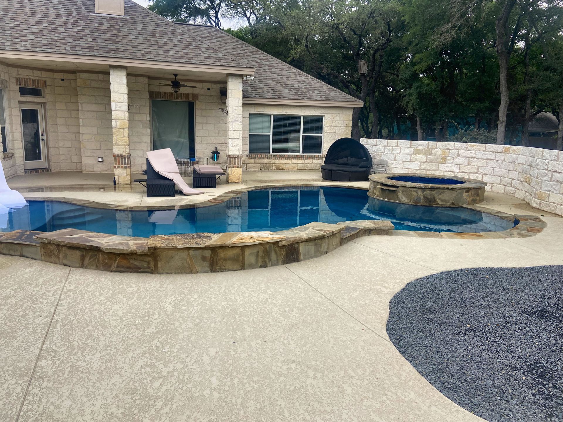 Swimming pool and hot tub with stone trim, patio furniture, and a backyard setting.