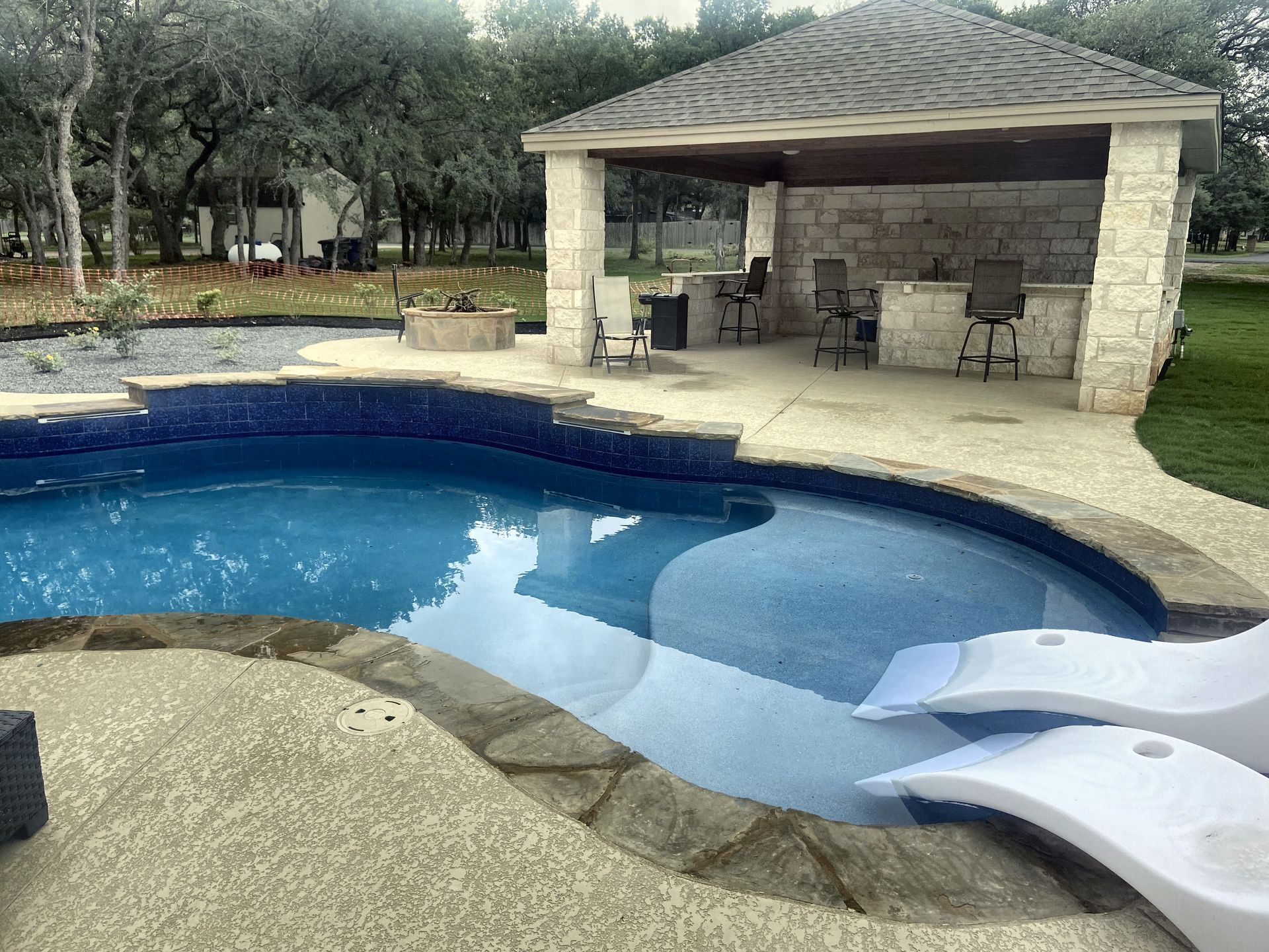 Swimming pool with blue tile and swim-up chairs, next to a stone patio with a covered bar area.