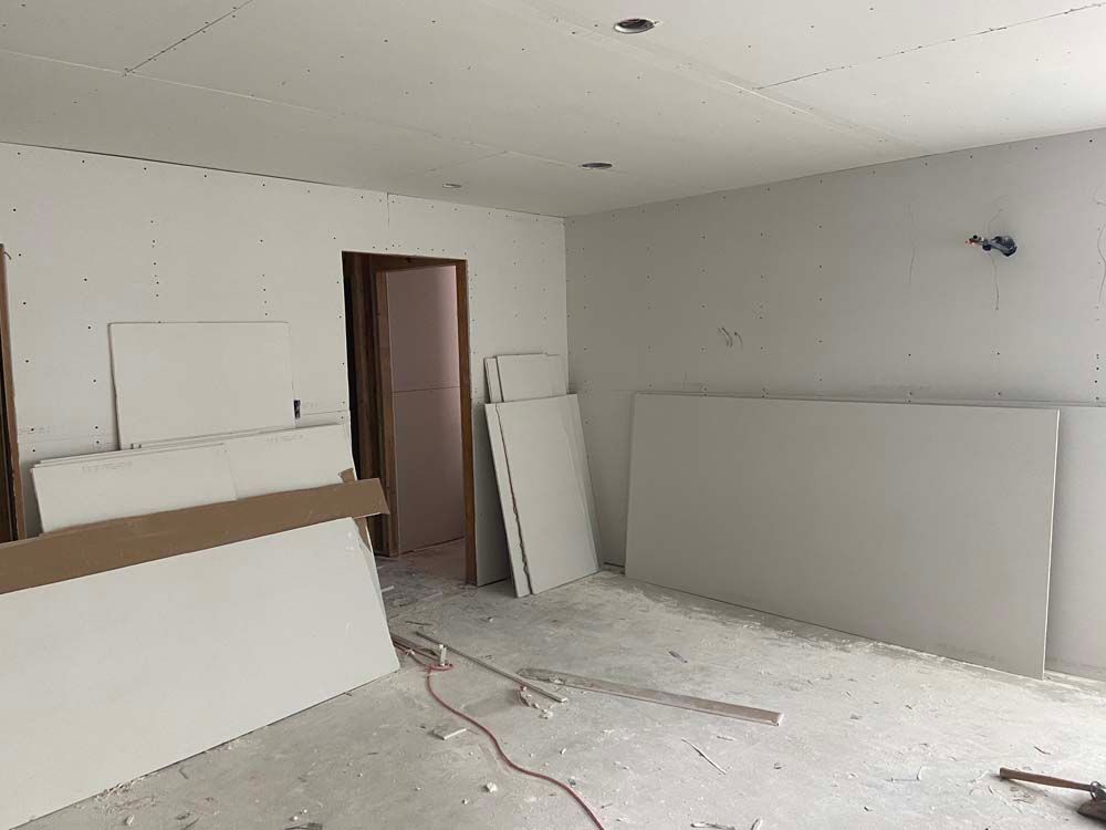 Room under construction with drywall sheets stacked against walls and on floor. Doorway visible.
