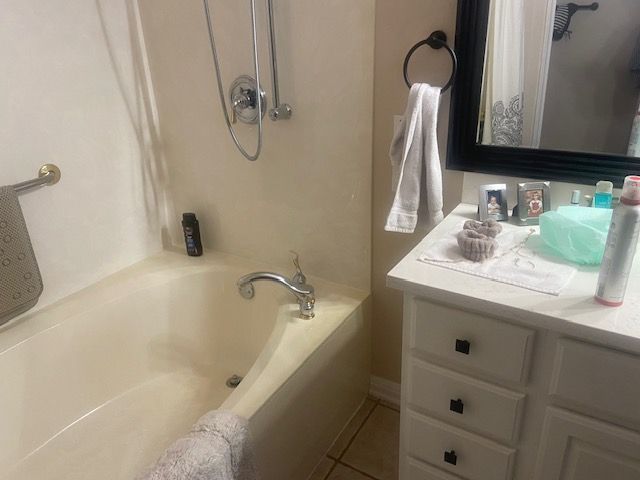 Bathroom with bathtub, sink, and a mirror. Beige and white tones with items on the countertop.