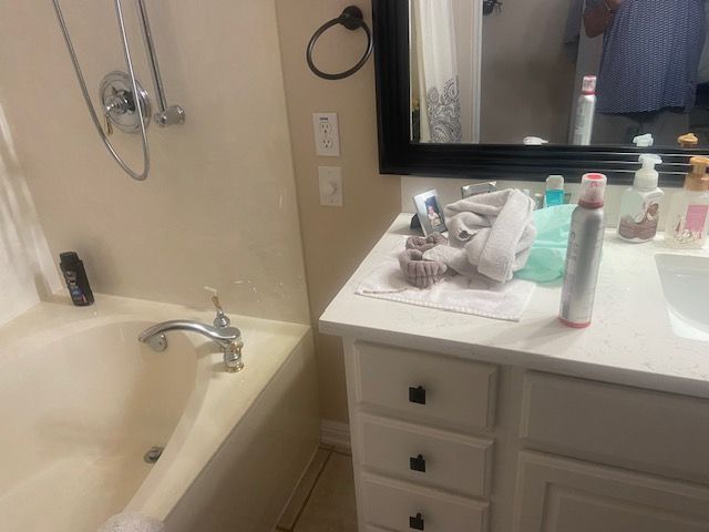 Bathroom with tub, vanity, and mirror. Soaps, towels, and a person reflected in the mirror.