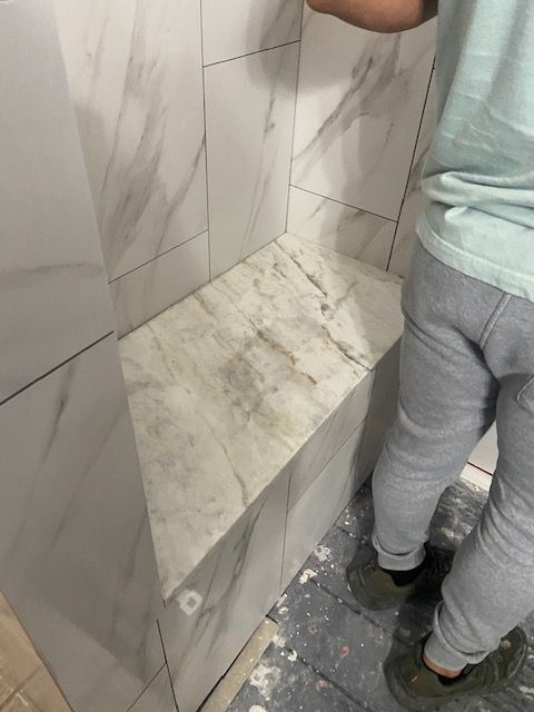 Person installing marble tile in shower with built-in corner seat.