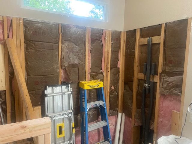 Interior wall under construction with insulation, ladder, and pipes.