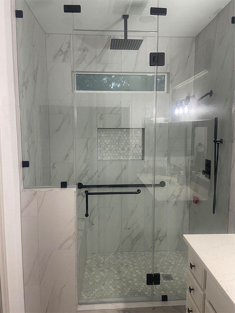Modern shower with marble-look tile, glass doors, dark hardware, and a rain shower head.
