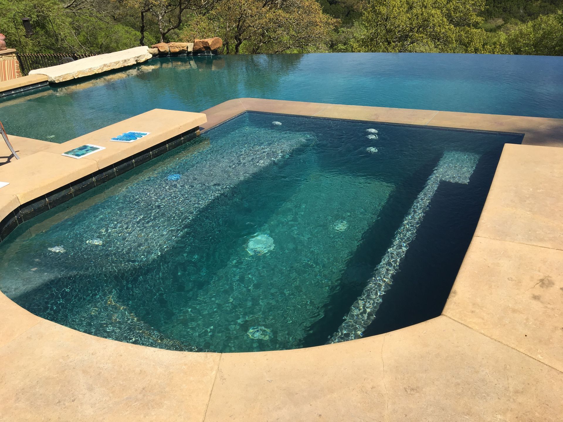 A two-tiered pool with an infinity edge, emerald water, and tan concrete surround.