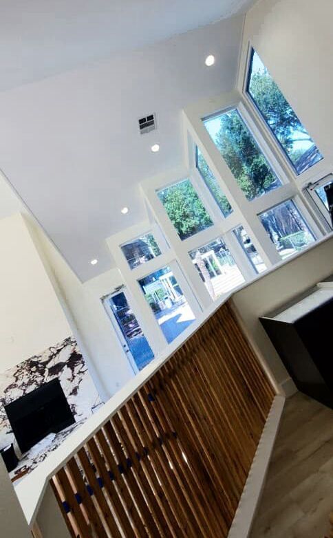 Interior view of a home with high ceilings, large windows, a wooden railing, and a fireplace.
