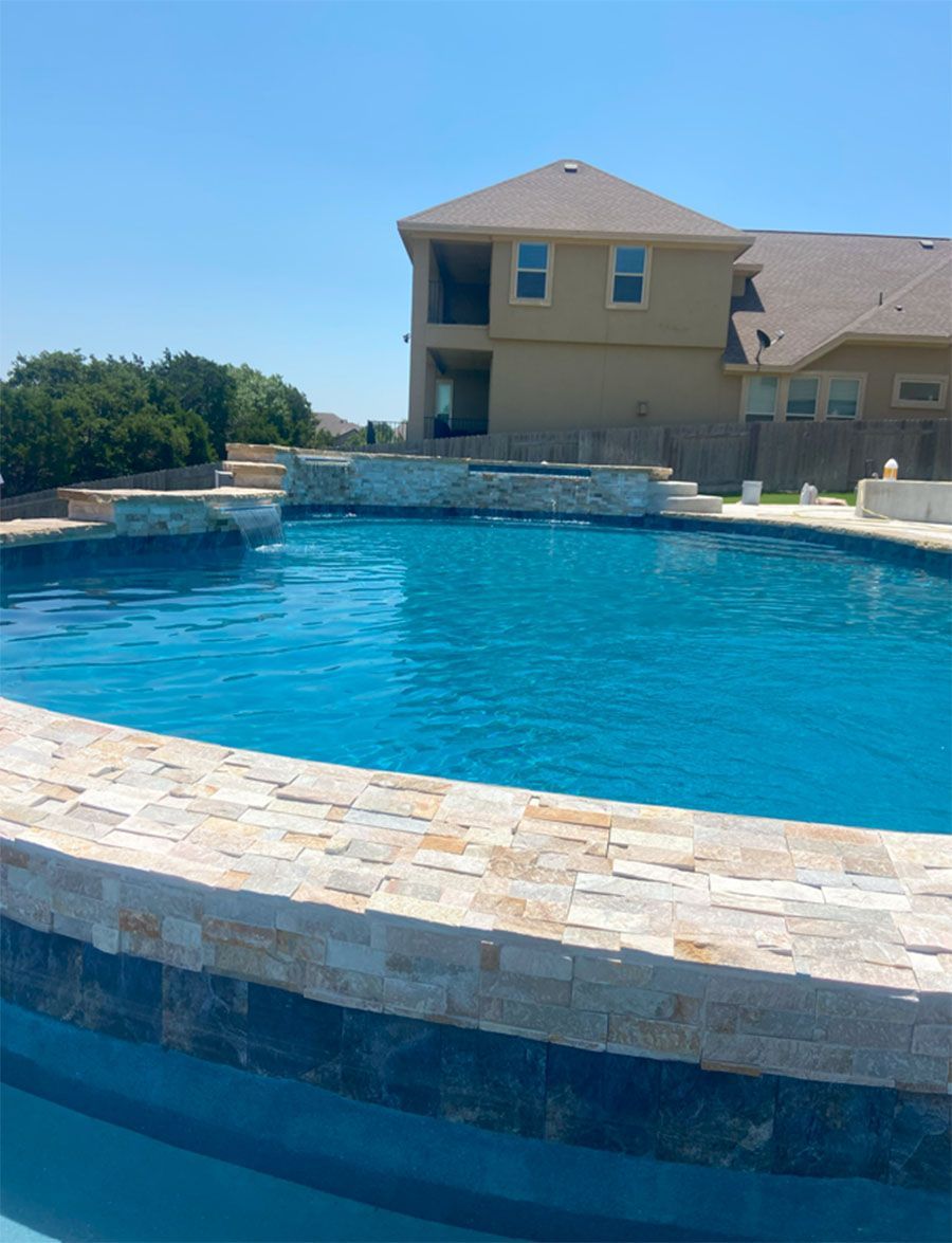 Swimming pool with stone border in front of a two-story house on a sunny day.