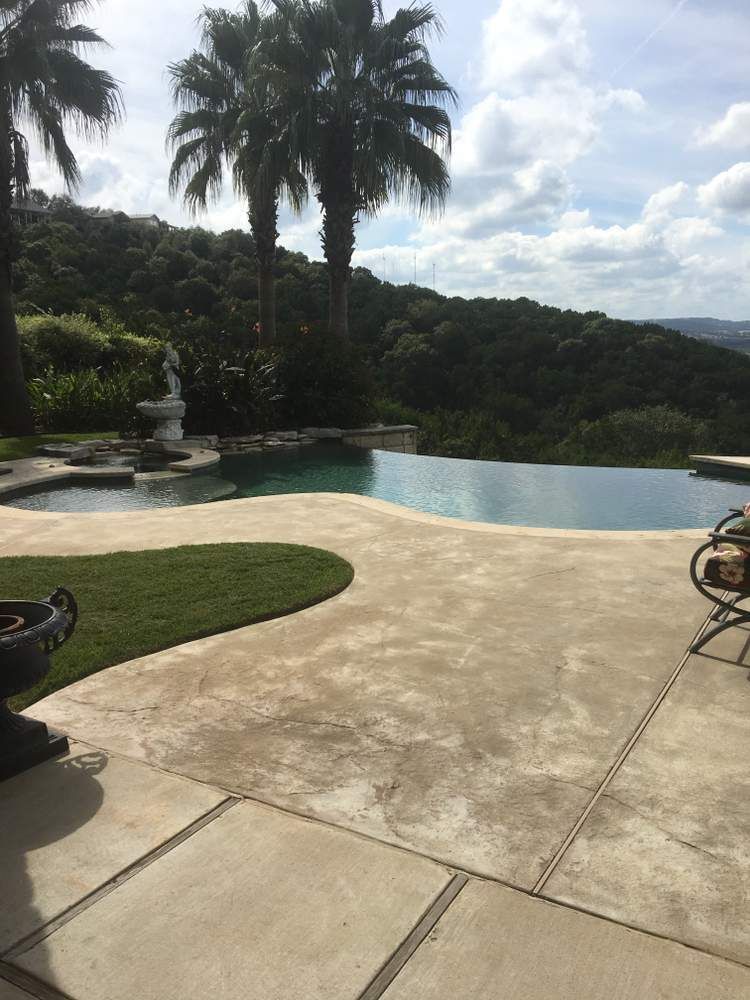 Pool with infinity edge overlooking a lush green hillside under a cloudy sky.