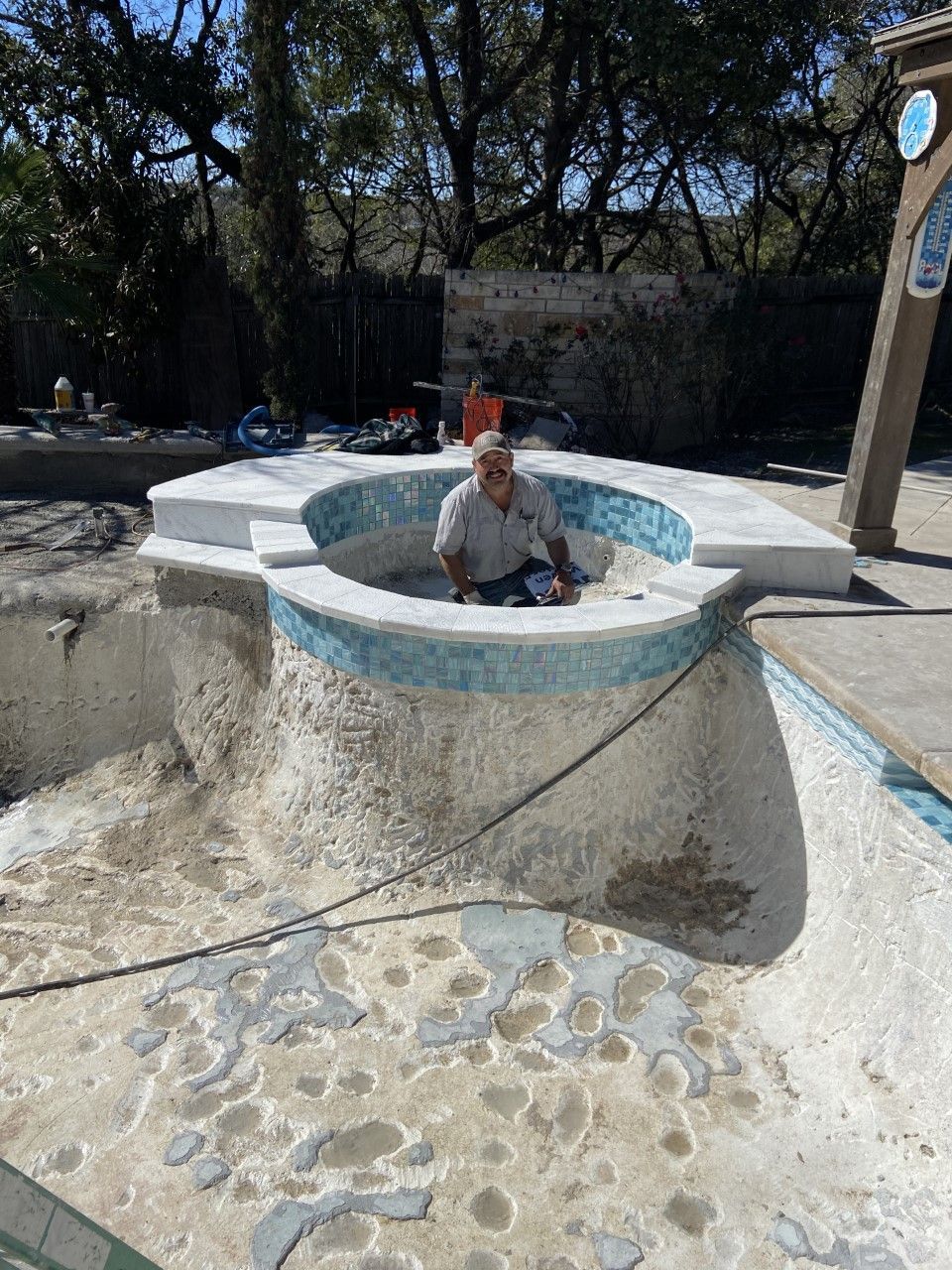 Man in a pool under construction; white, gray, and blue tiles. Outdoors.