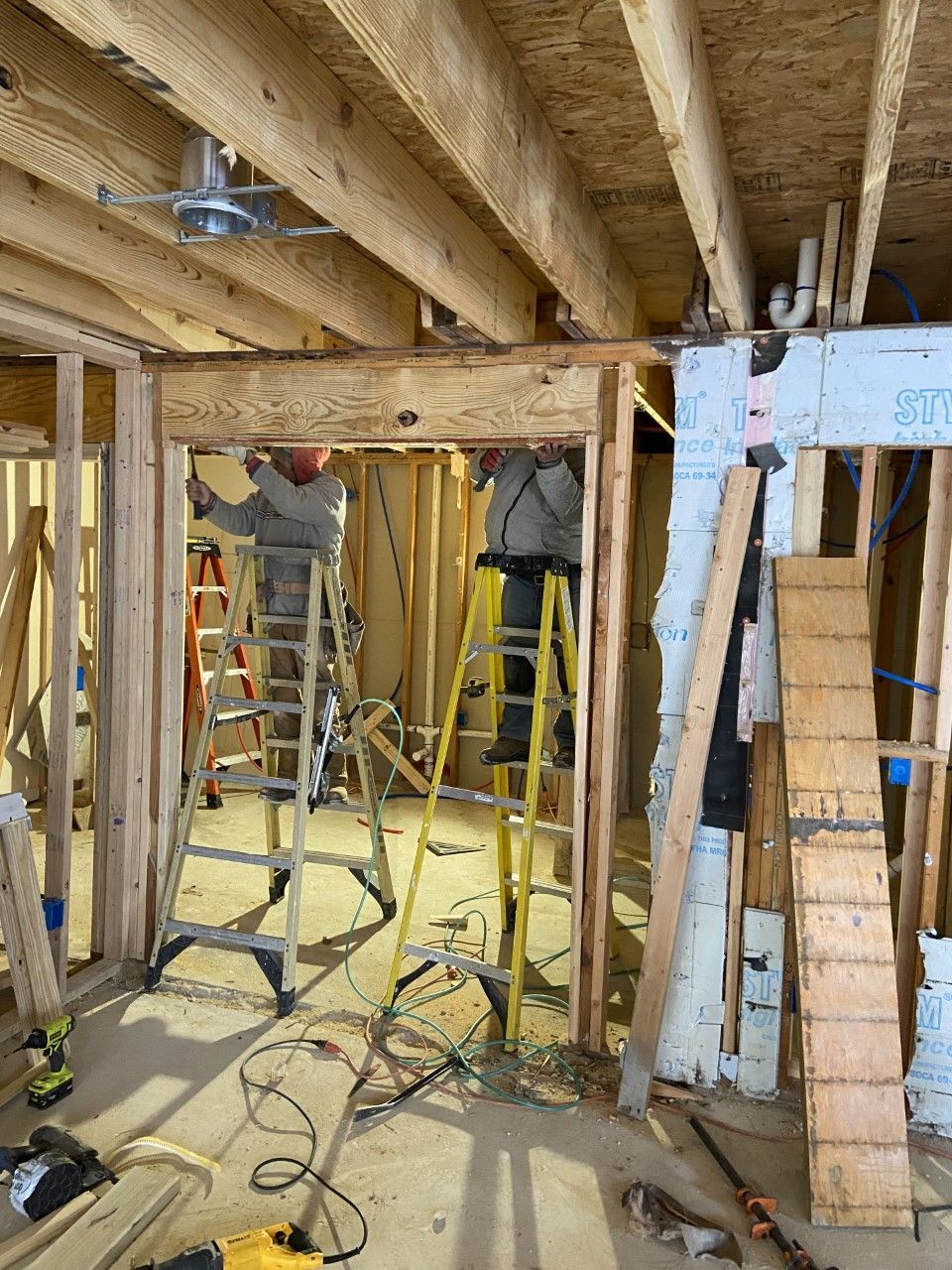 Two people on ladders frame a doorway in a wood-framed building under construction.