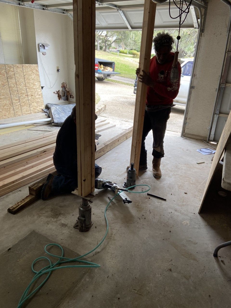 Two people building a structure in a garage, using lumber and tools.