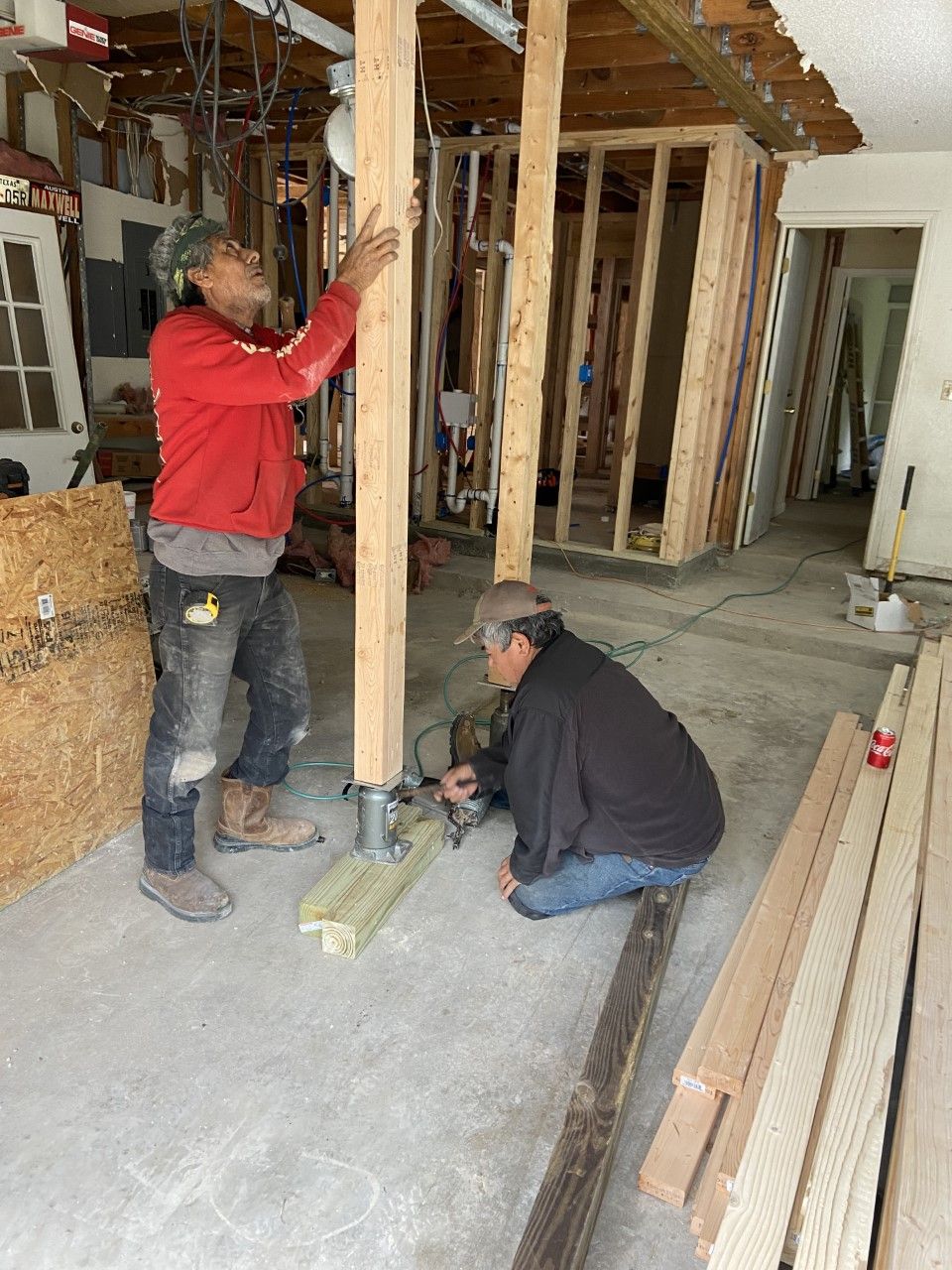 Two men building wooden support beams inside a room under construction.