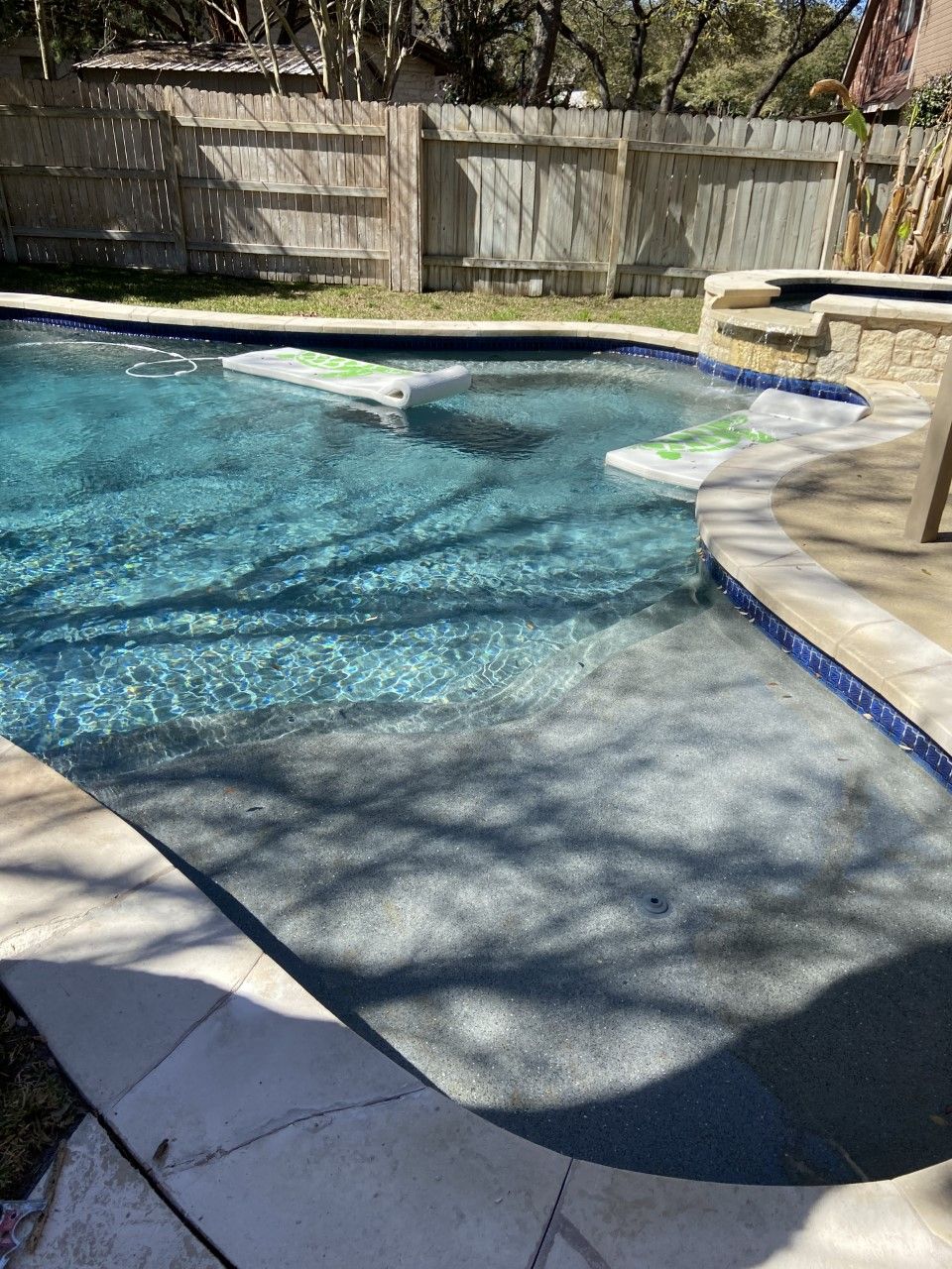 A blue tiled swimming pool with steps, surrounded by a patio and wooden fence.