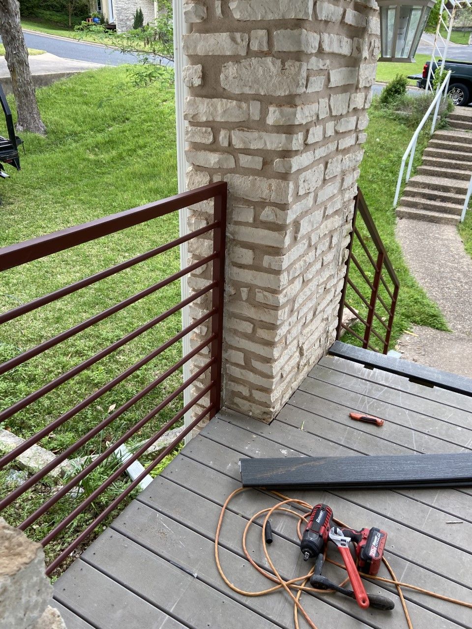 Brick pillar with red metal railing on a composite deck; tools are present.