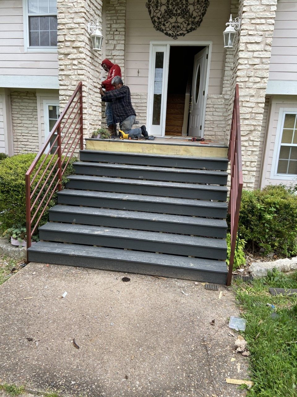 People working on steps leading to a house with an open door. Gray steps and brick exterior.