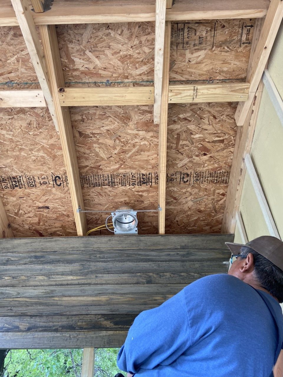 Person looking up at exposed wood ceiling with electrical box installed.