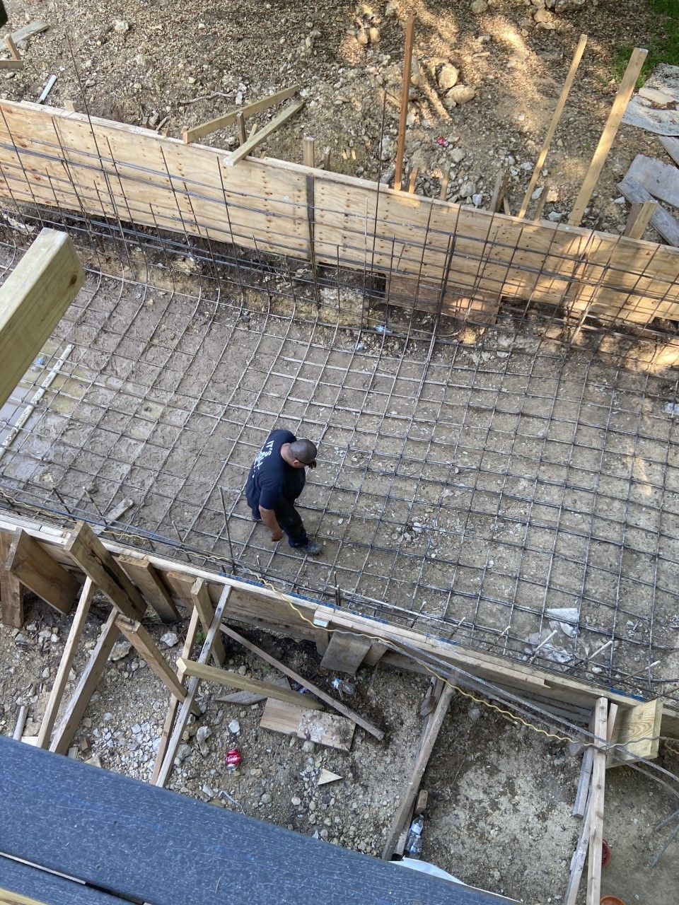 Construction site: A worker stands within wooden forms and rebar, preparing for concrete pouring.