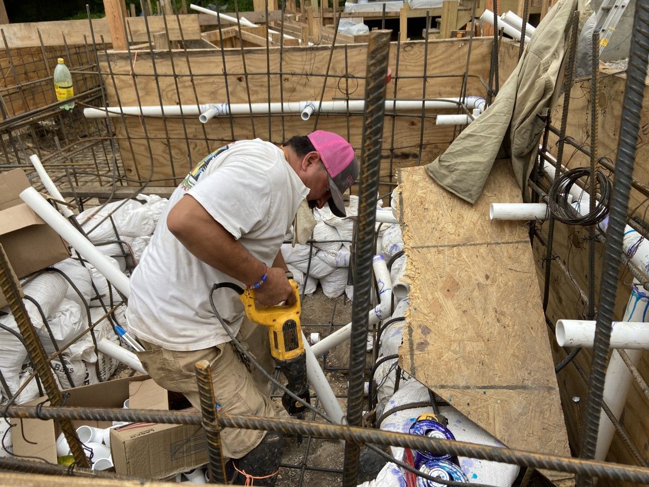 Construction worker cutting a PVC pipe with a power saw, amid concrete reinforcement and formwork.