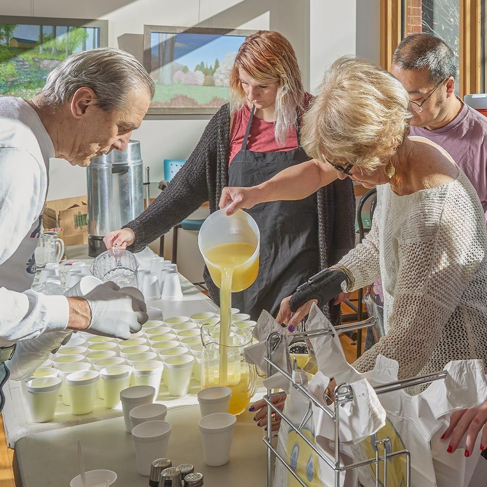 A group of people are pouring orange juice into cups