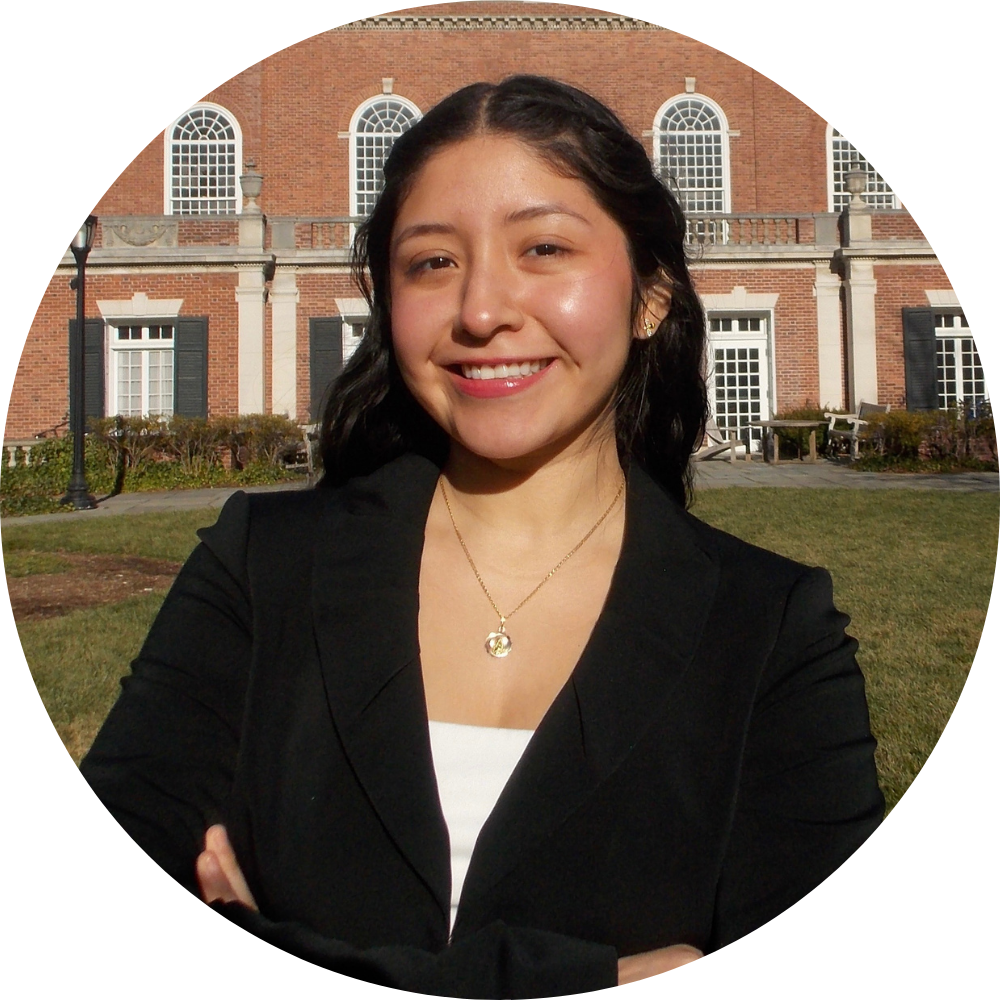 A young man wearing glasses and a blue shirt is smiling in a library.