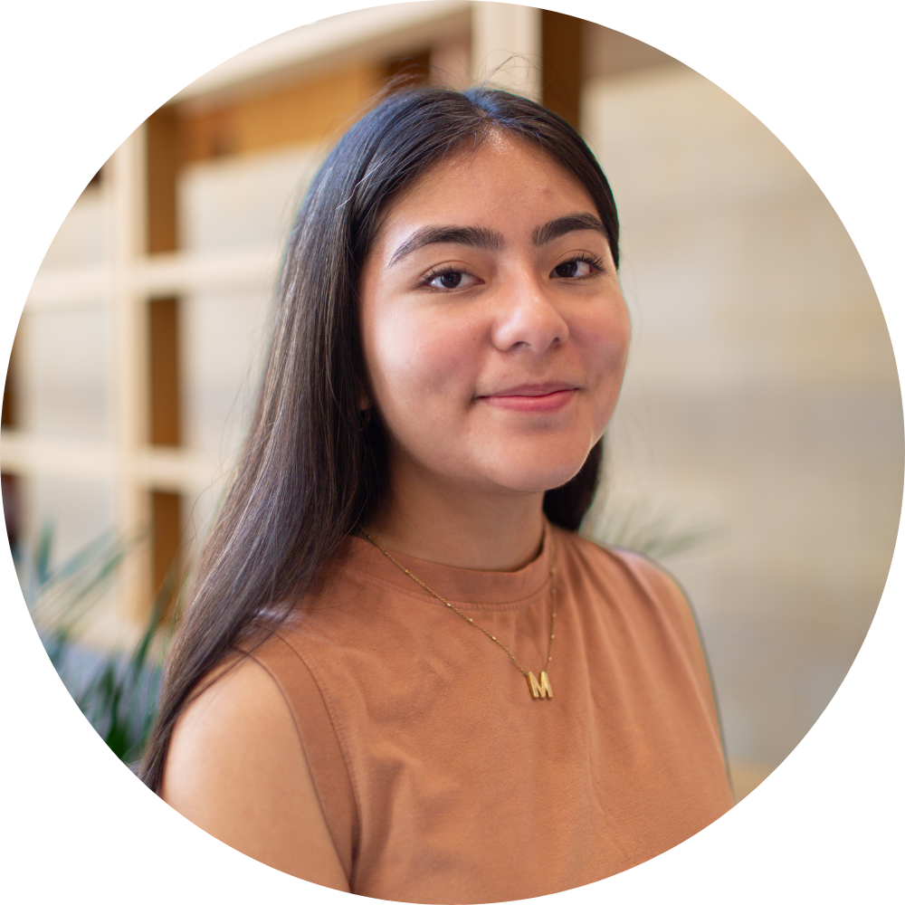 A woman wearing a black jacket and a gold necklace is smiling for the camera.