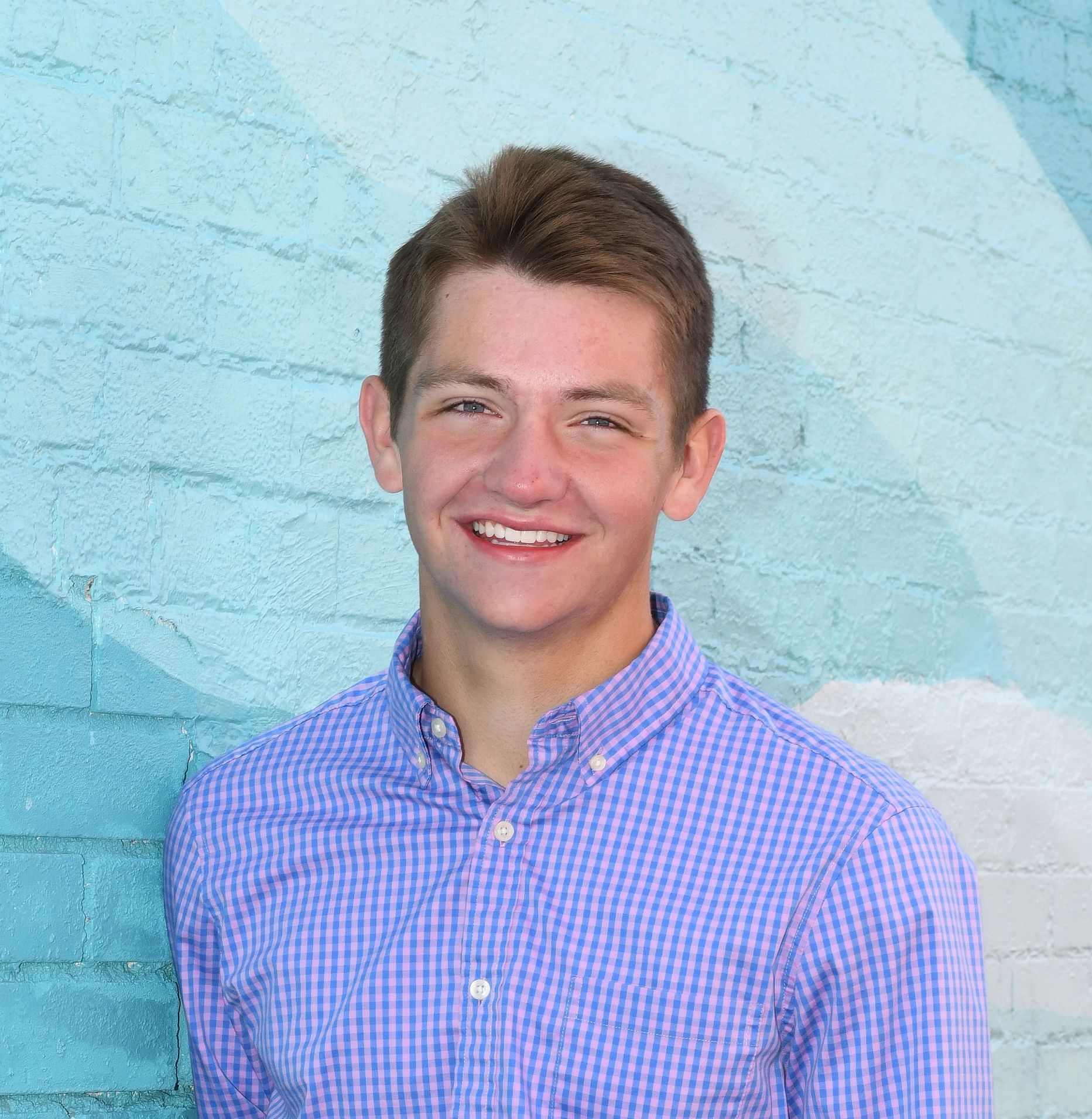 A young man wearing glasses and a blue shirt is smiling in a library.