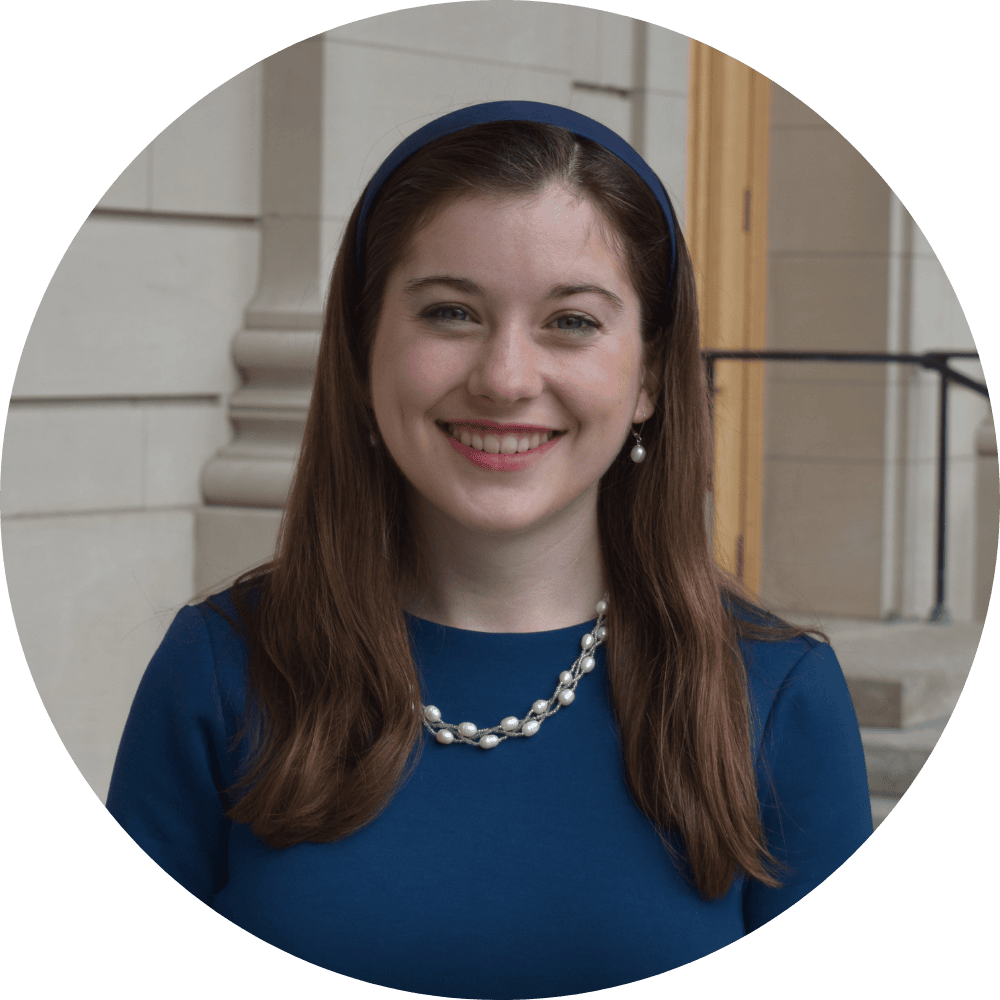 A young man wearing glasses and a blue shirt is smiling in a library.