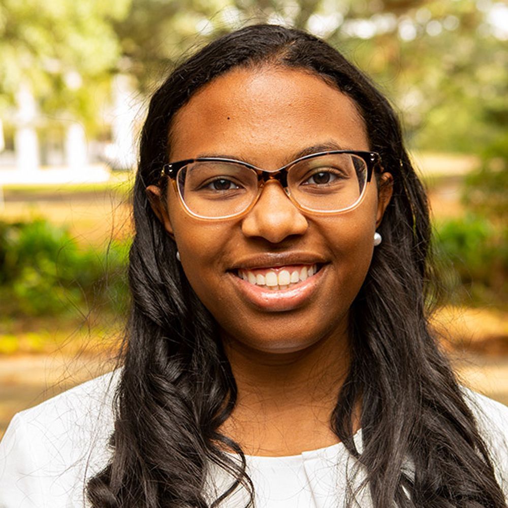 A woman wearing glasses and a white shirt is smiling for the camera.