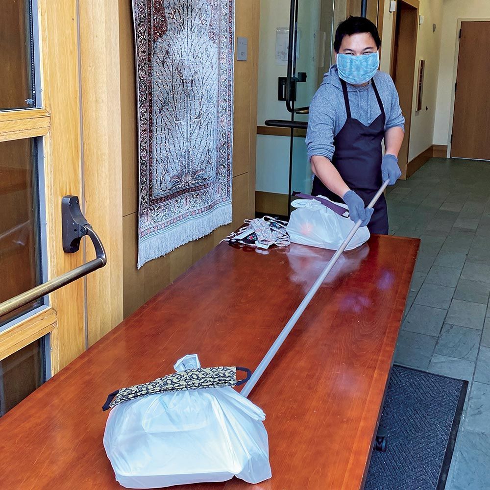 A man wearing a mask is cleaning a table with a mop