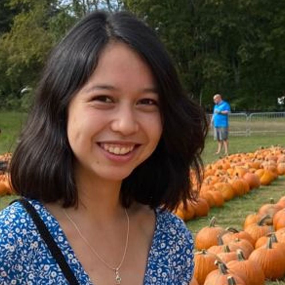 A woman is smiling in front of a field of pumpkins.