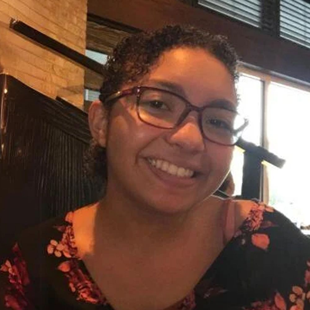 A woman wearing glasses and a floral shirt is smiling for the camera.