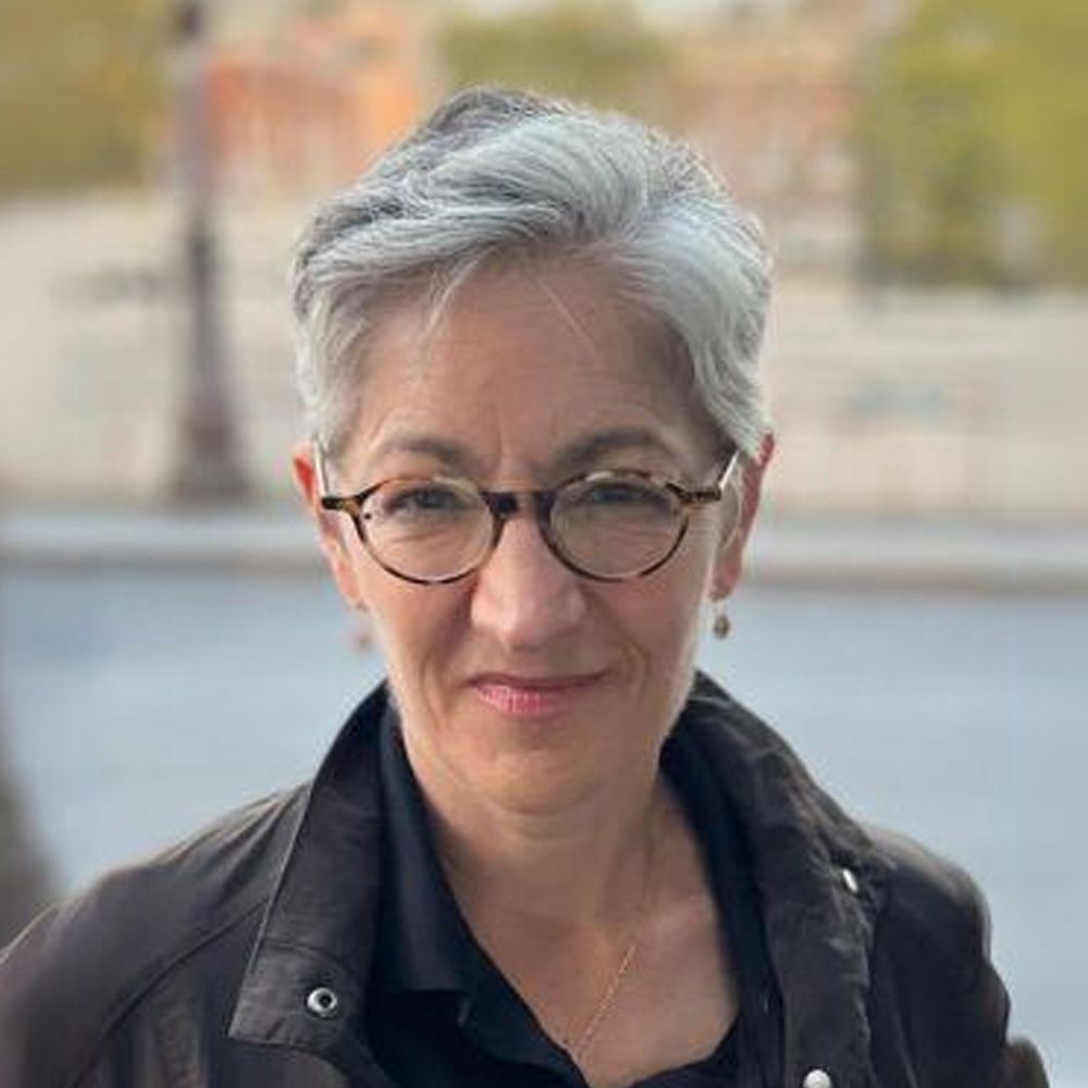 A woman wearing glasses and a black jacket is smiling for the camera.