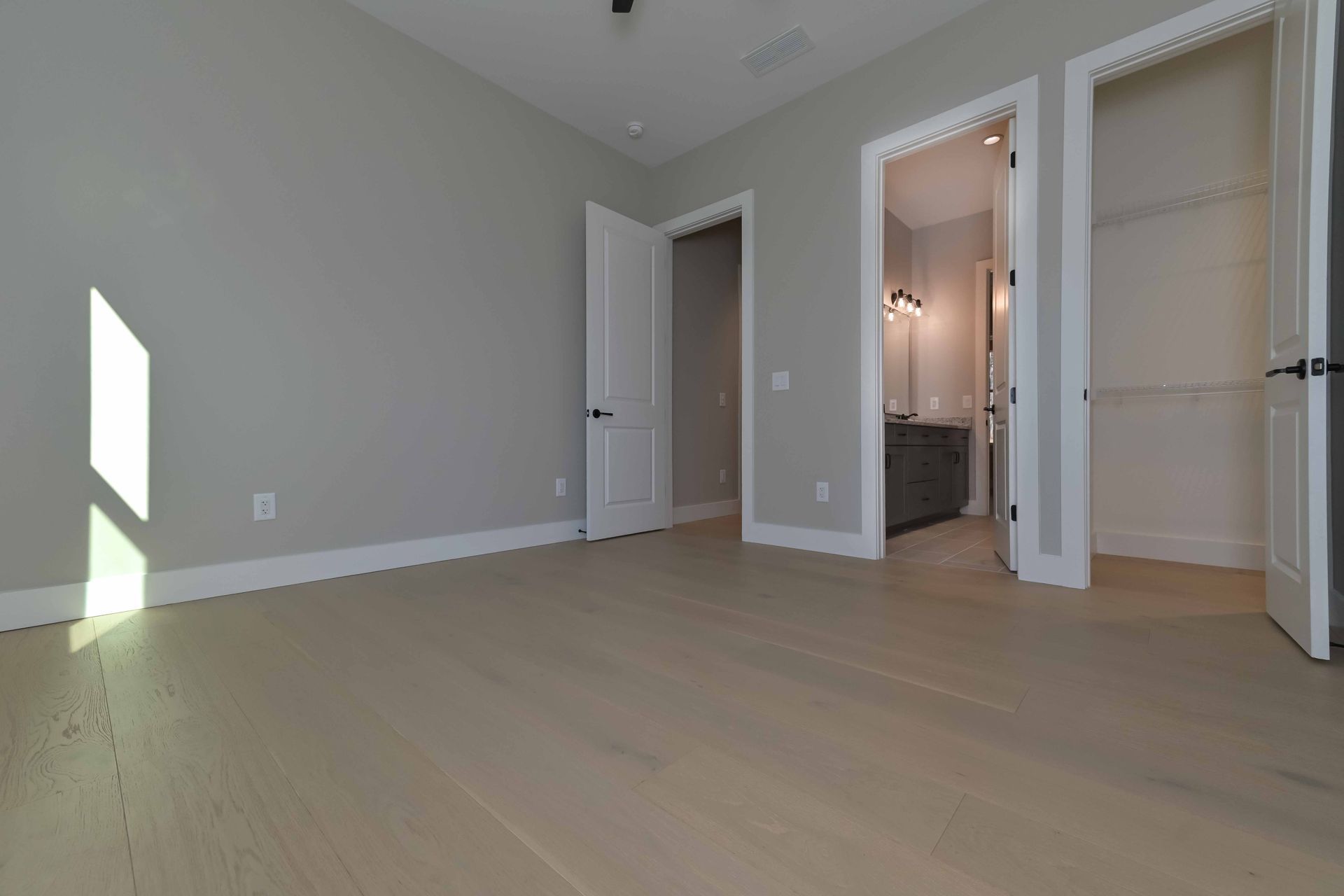 An empty bedroom with hardwood floors and a bathroom.