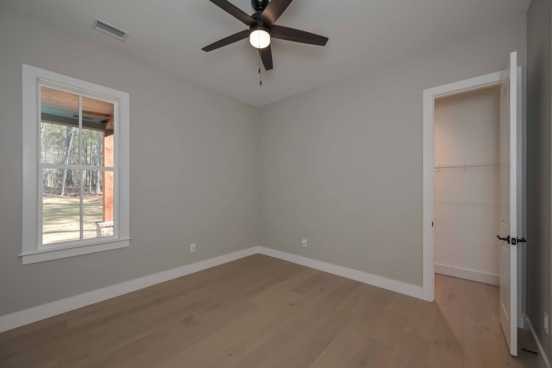 An empty bedroom with a ceiling fan and two windows.
