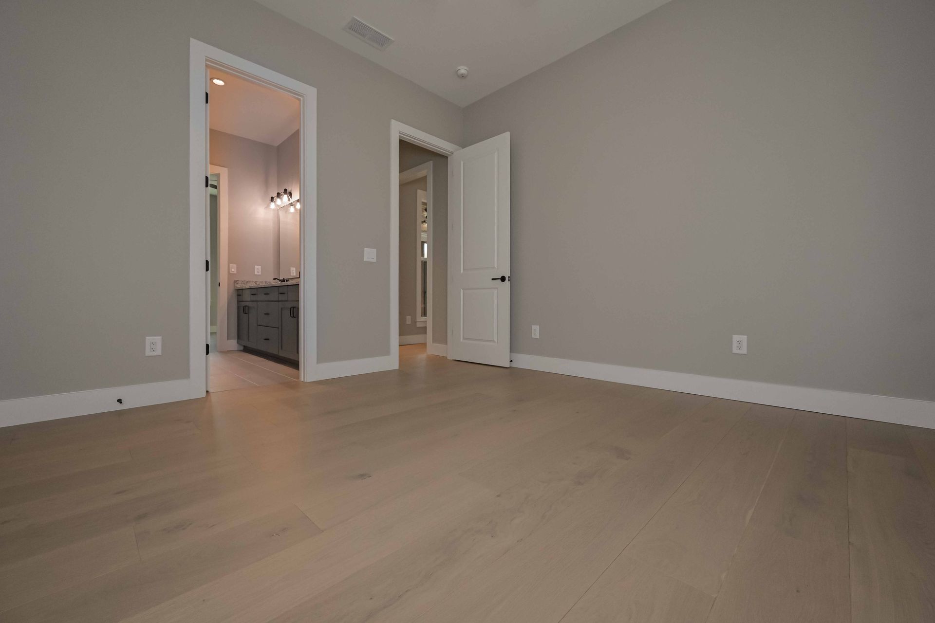 An empty bedroom with hardwood floors and gray walls.