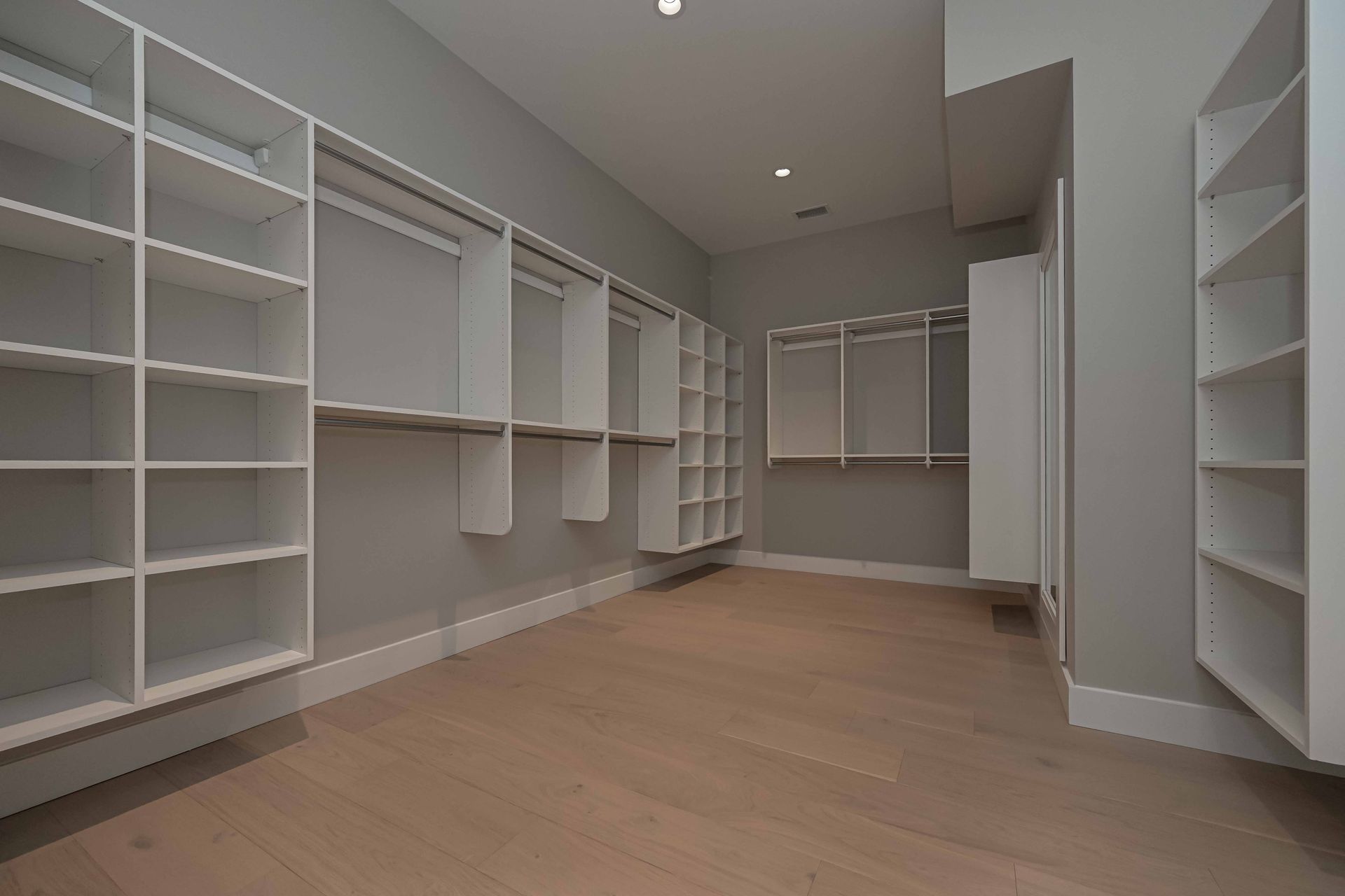 An empty walk in closet with lots of shelves and a wooden floor.