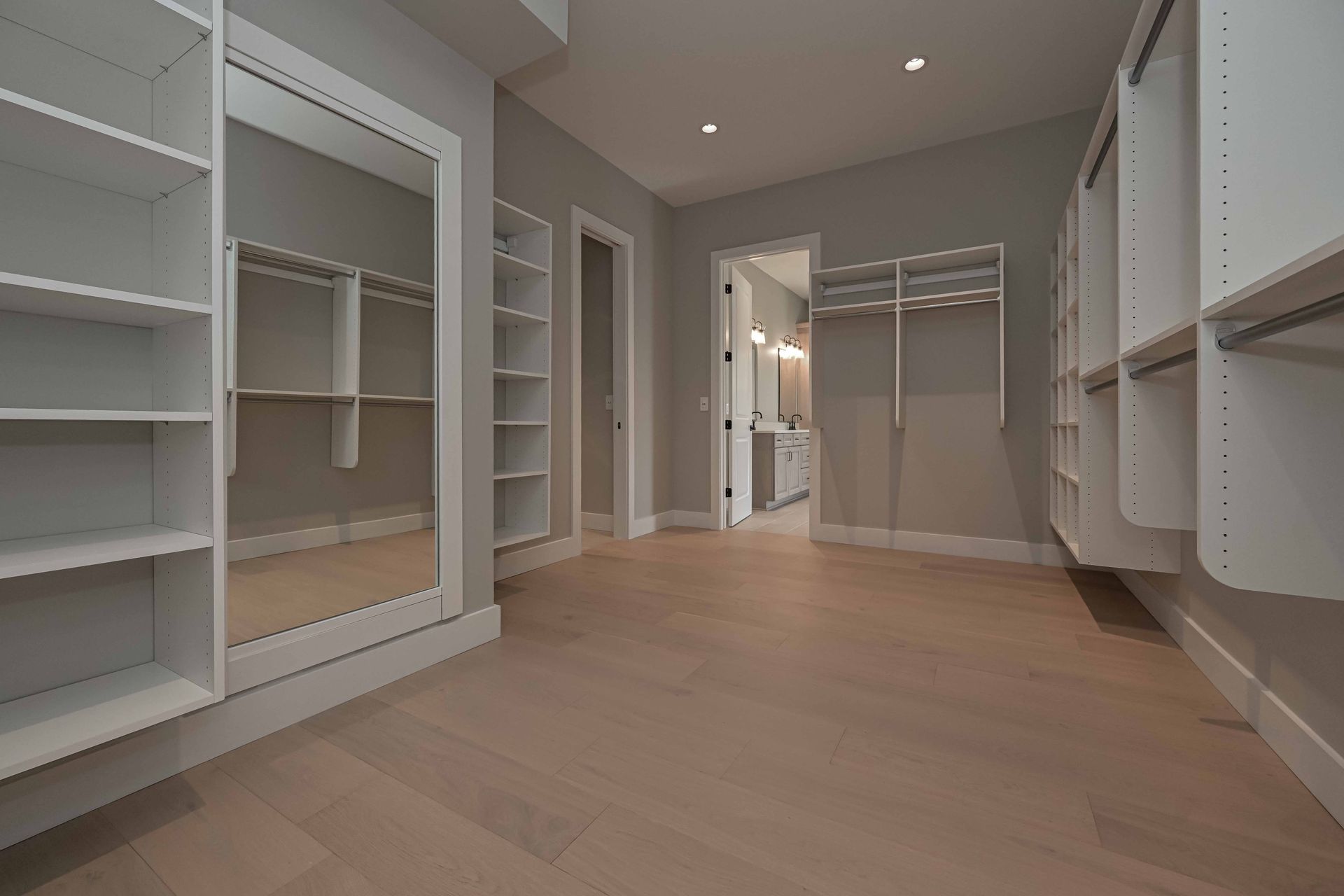 An empty walk in closet with lots of shelves and mirrors.