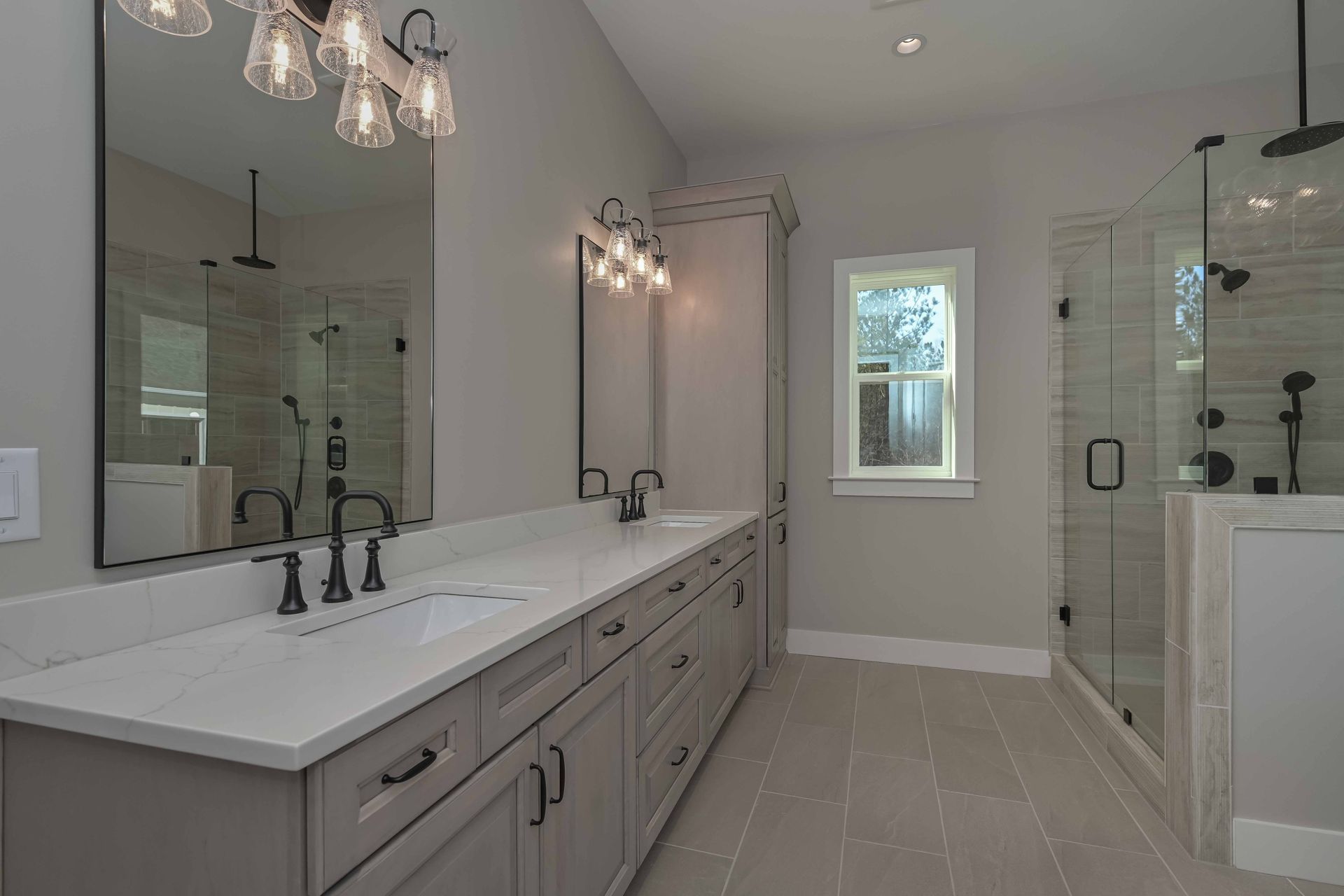A bathroom with two sinks , two mirrors , and a walk in shower.