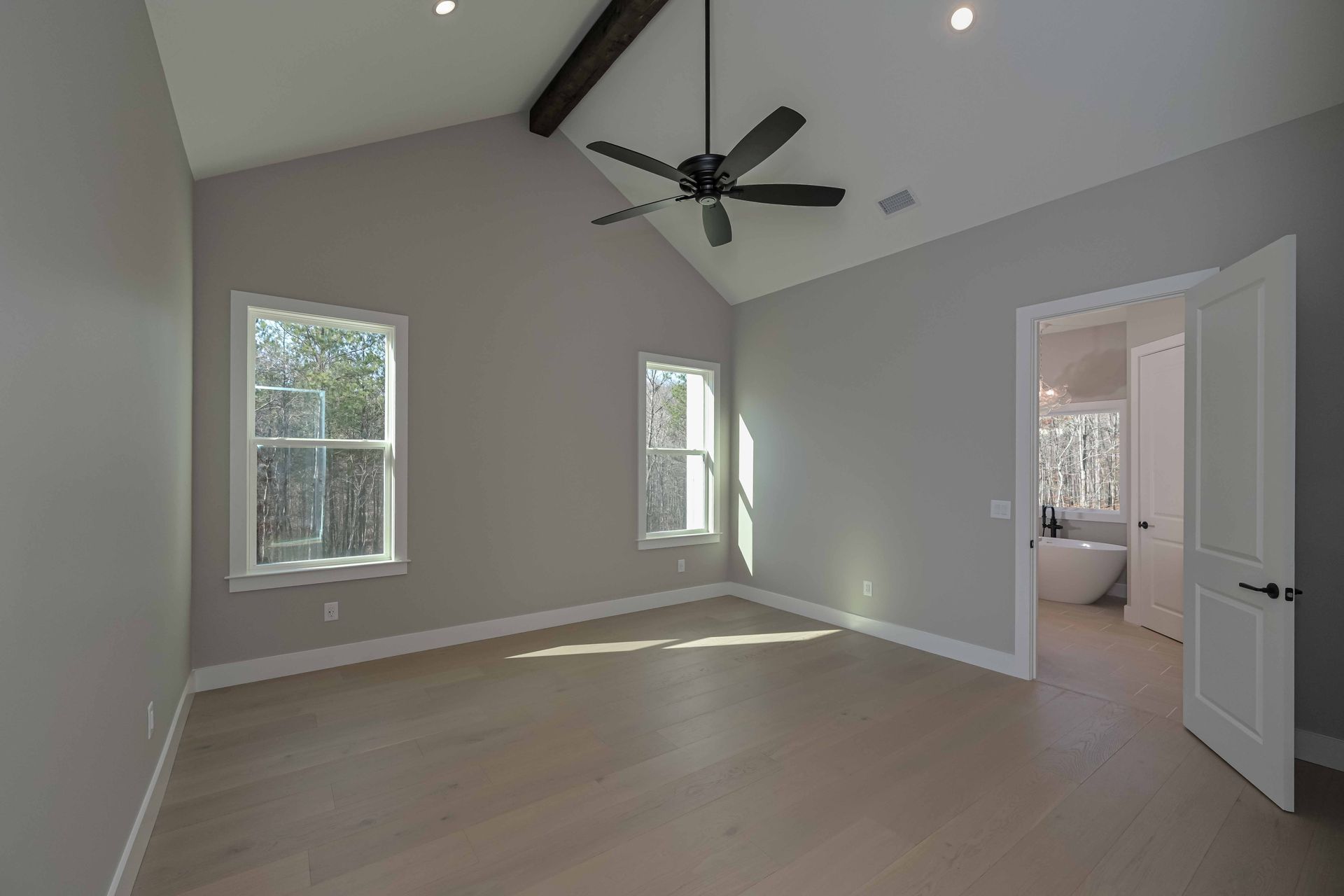 An empty bedroom with a ceiling fan and two windows.