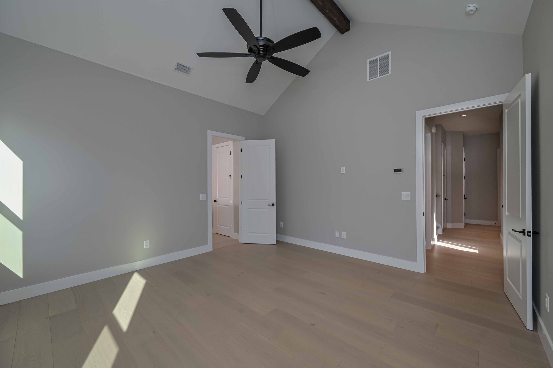 An empty bedroom with a vaulted ceiling and a ceiling fan.