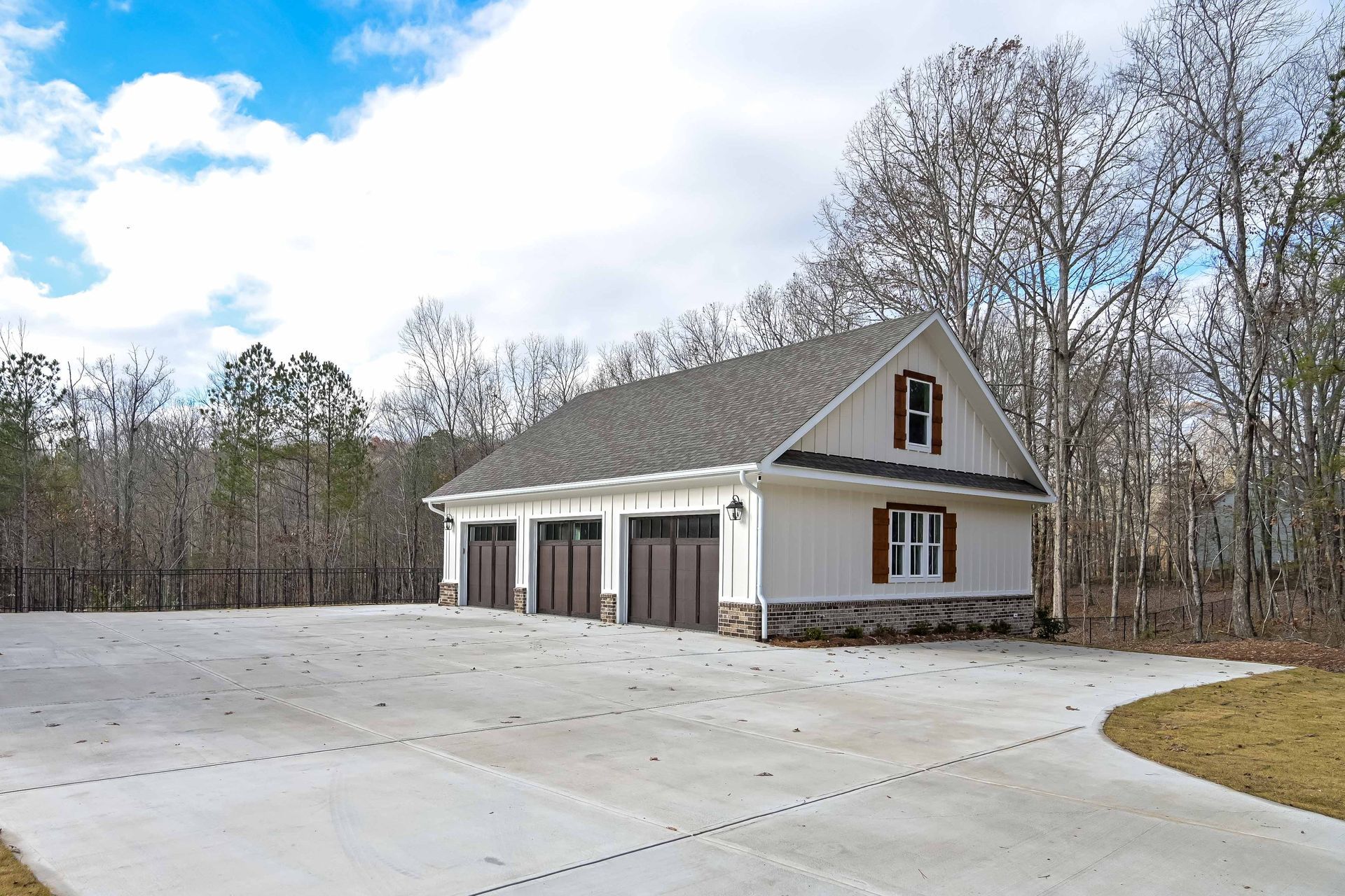 A large white garage with three garage doors is surrounded by trees and a concrete driveway.