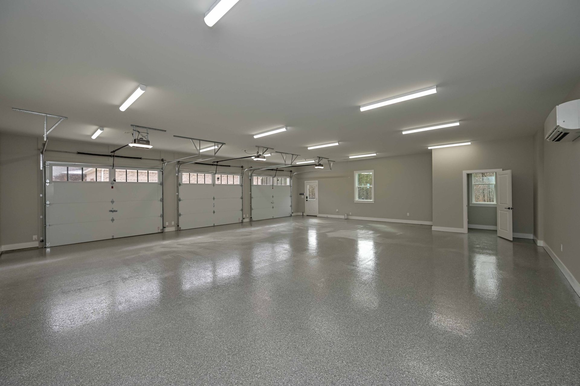 A large empty garage with a gray floor and white garage doors.