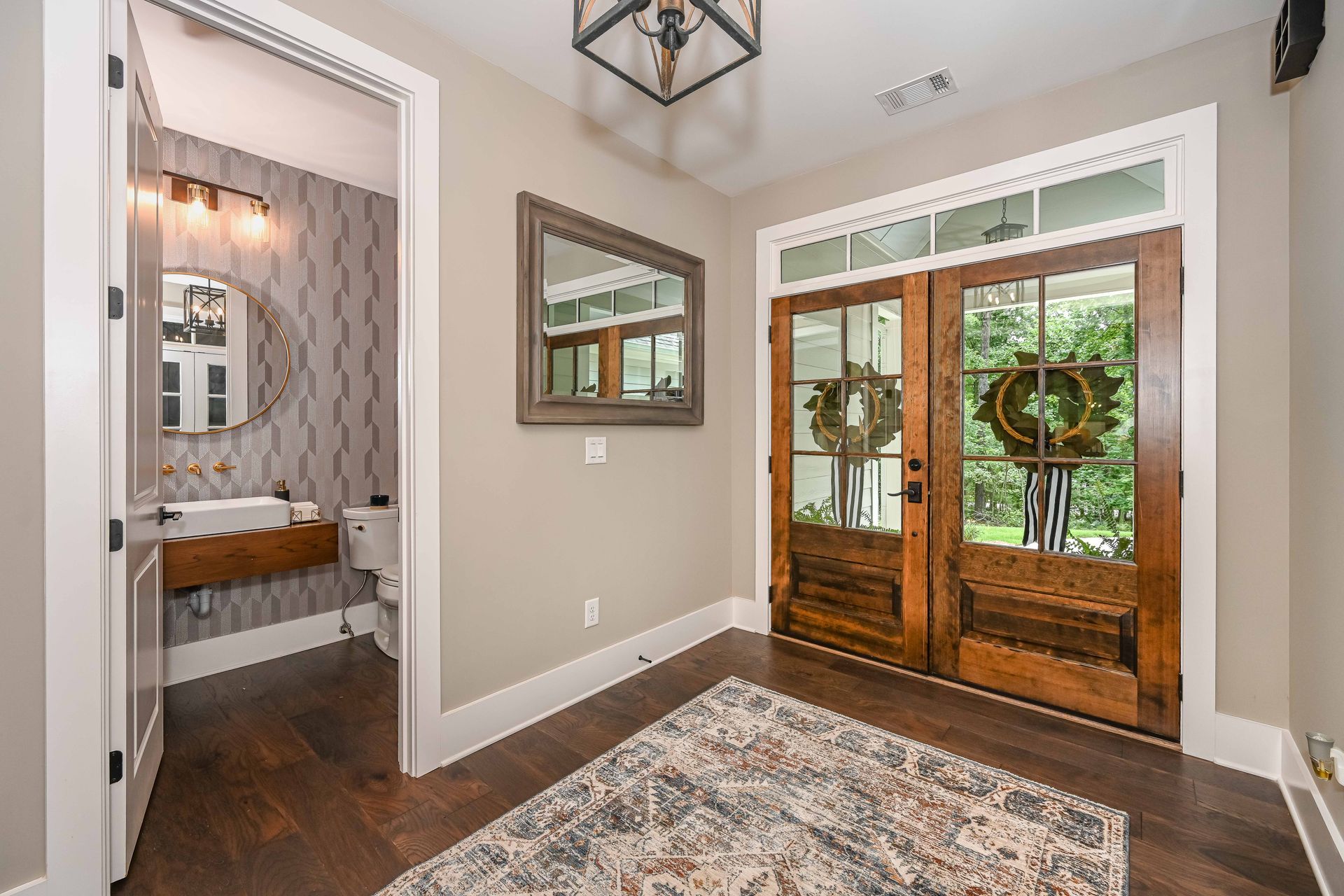 A hallway with a rug , mirrors , and a bathroom.