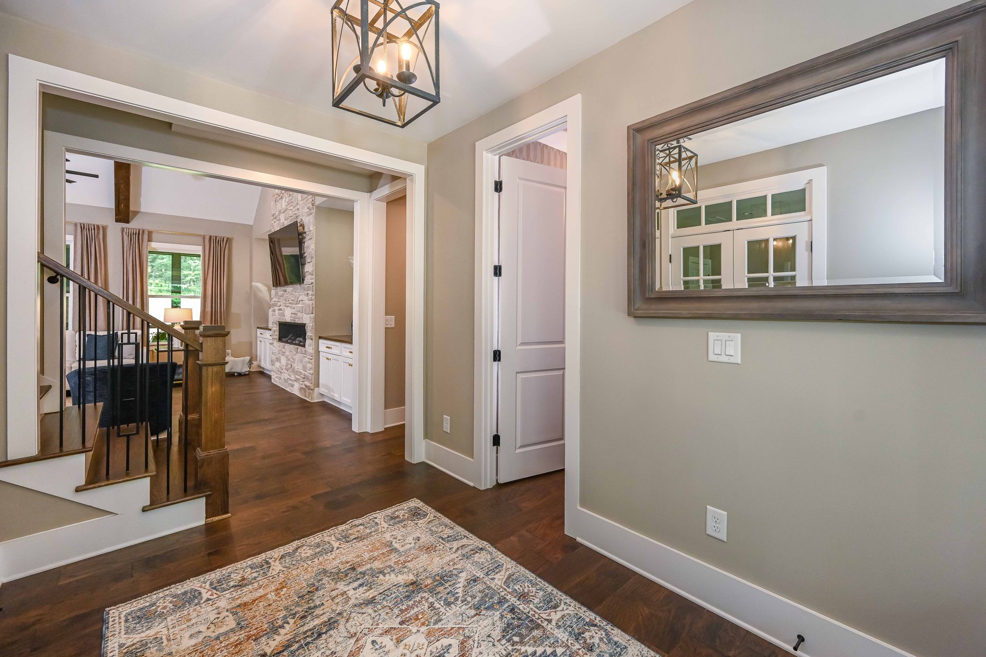 A hallway with a rug , mirror and stairs in a house.