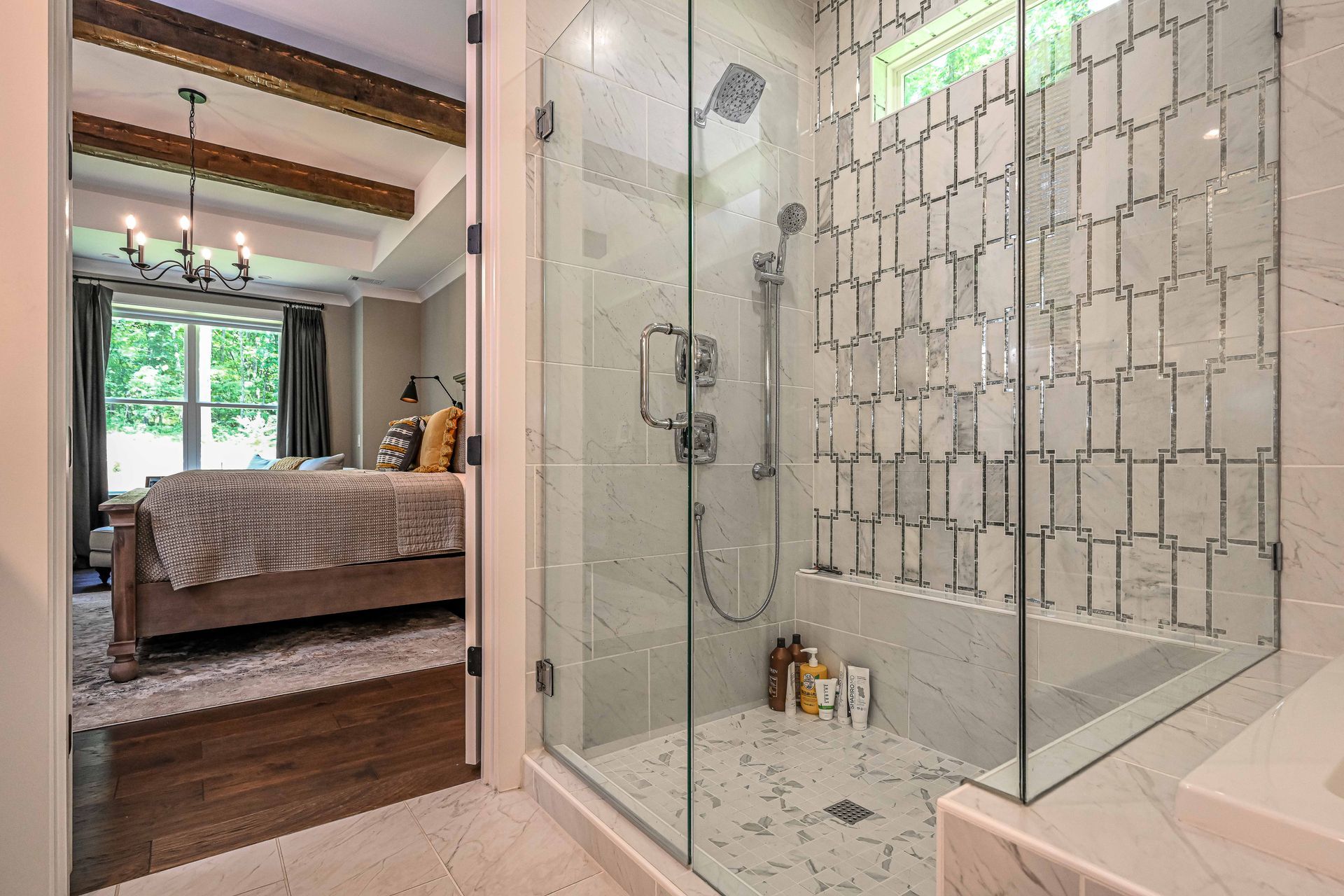 A bathroom with a walk in shower and a bed in the background.